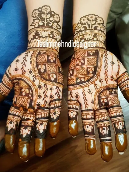 This intricate design uses checkered patterns and leafy vines to create a full and detailed look. The dark fingertips are a classic element in traditional mehndi.