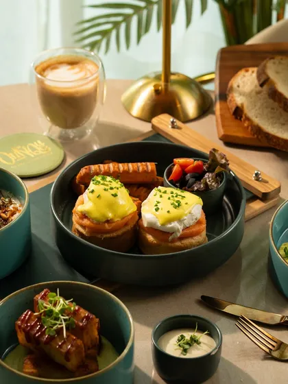 A close-up of a brunch platter featuring eggs benedict and sausages. The tight crop makes the food the hero.