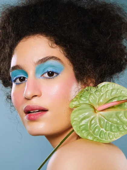 A vibrant floral-inspired look with a bold block of blue eyeshadow, contrasted with a fresh green anthurium flower.