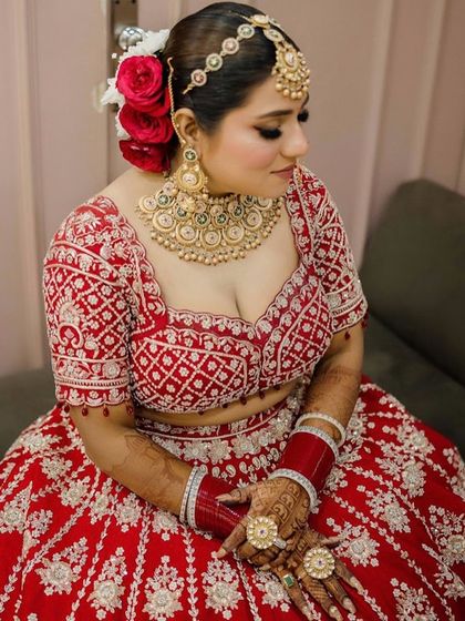 A beautiful seated portrait of the bride, showcasing her full red lehenga and the classic makeup look. The winged liner and soft blush complete this elegant bridal style.