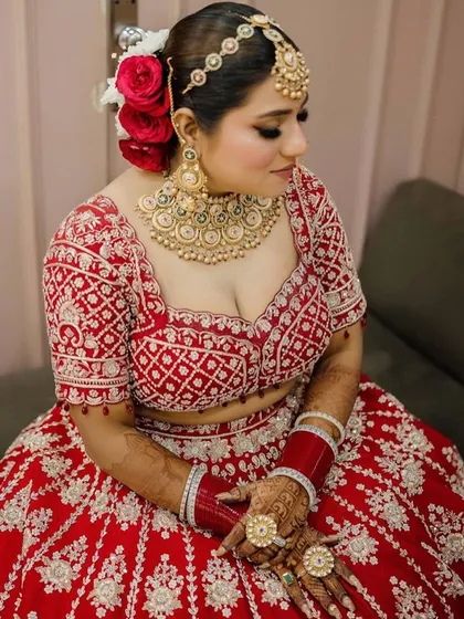 A beautiful seated portrait of the bride, showcasing her full red lehenga and the classic makeup look. The winged liner and soft blush complete this elegant bridal style.