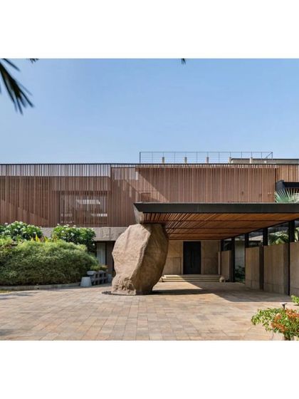 The dramatic entrance of the K House, featuring a massive natural boulder that anchors the structure to its site. This project in Alibag is a powerful example of tropical modernity and sensitive reinvention.