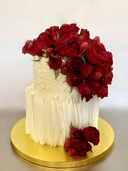 A timeless and elegant two-tiered wedding cake. The combination of a textured white finish, fresh red roses, and raspberries creates a look of pure romance, perfect for an anniversary or engagement.
