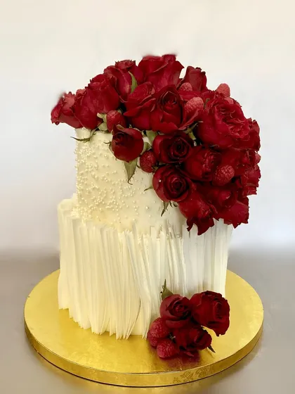 A timeless and elegant two-tiered wedding cake. The combination of a textured white finish, fresh red roses, and raspberries creates a look of pure romance, perfect for an anniversary or engagement.