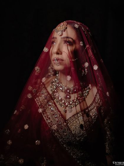 A stunning portrait of the bride under her veil, with dramatic lighting highlighting her features and jewelry.