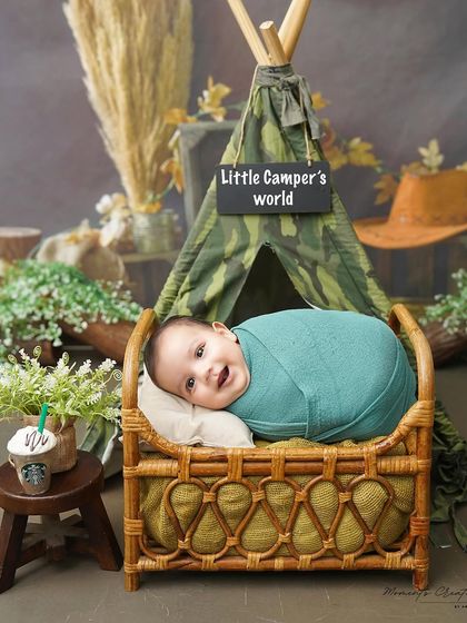 A cozy and happy little camper. Swaddled and snug in a miniature bed, this three-month-old is all smiles during his camping-themed milestone session.