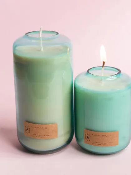 The Volumetric Curve candle in a serene Bahama Breeze scent and a cool minty green color. The smaller candle is lit, showcasing the beautiful glow through the colored glass.