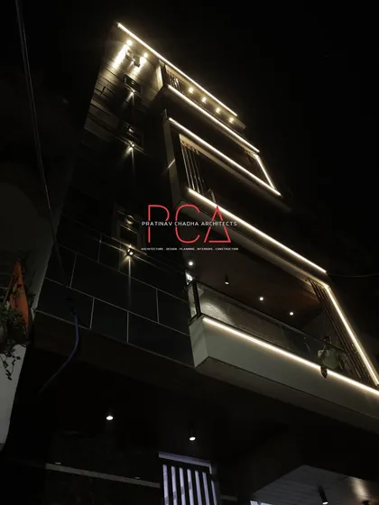 An upward-angle shot of 'The Cursive Abode' facade at night. The linear lighting traces the architectural frames, creating a sense of depth and luxury while accentuating the building's verticality.