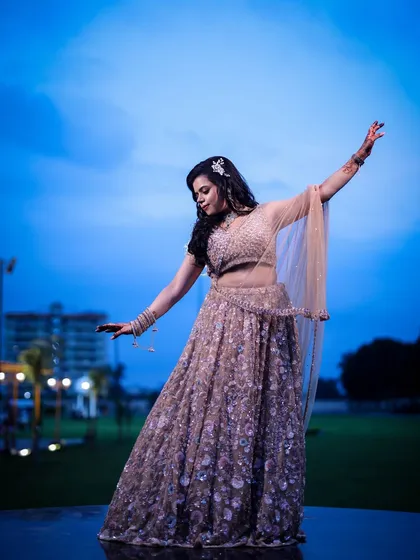 A woman strikes a graceful pose against the evening sky, her lehenga flowing around her.