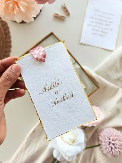 A close-up of the couple's names written in beautiful Copperplate calligraphy on handmade paper with a gilded edge.