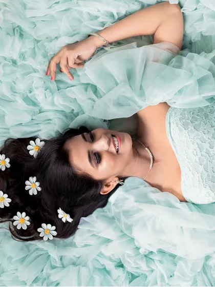 A beautiful overhead shot capturing a moment of pure bliss. The mom-to-be lies on a bed of soft blue tulle, with delicate flowers in her hair, creating an artistic and ethereal portrait.