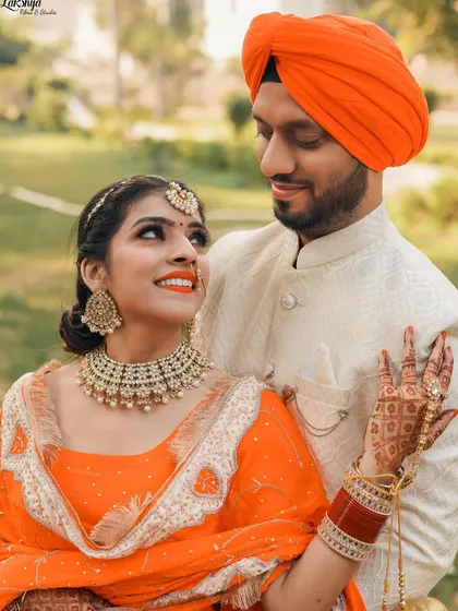 A classic pre-wedding portrait of a Punjabi couple. The bride's upward glance and the groom's loving look create a beautiful connection, highlighting their vibrant orange outfits.
