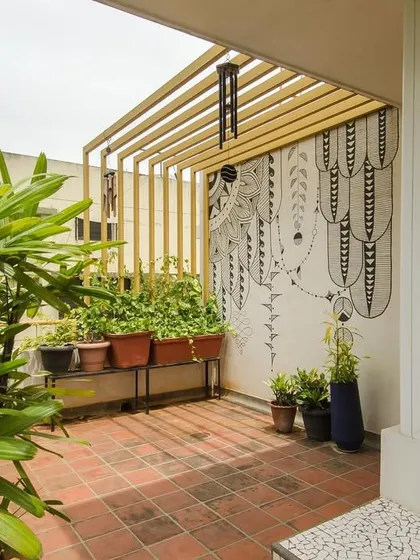 A black and white graphic mural provides a striking contrast to the vibrant plants on this terrace. A simple metal pergola adds structure and defines the space, creating a cozy and artistic outdoor nook.