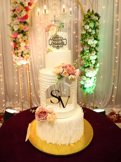 This grand four-tier engagement cake combines multiple textures for a truly unique look. From the smooth top tier with a 'Just Engaged' topper to the textured middle and ruffled bottom tiers, it's a statement piece for any large celebration.