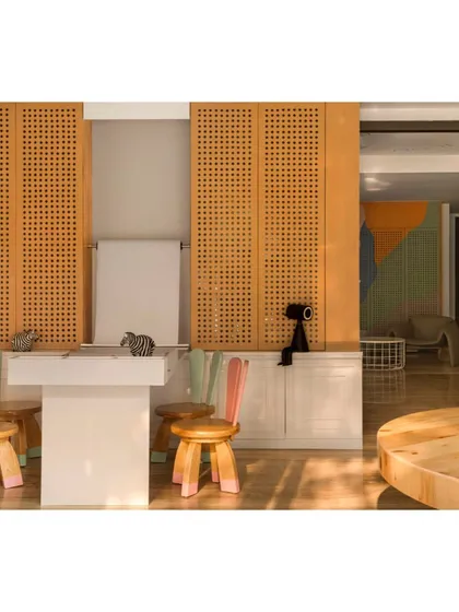 The activity corner in the clinic features child-sized chairs with playful, rabbit-ear backs and a table for drawing. The perforated wooden screens and a roll of paper invite creative expression.