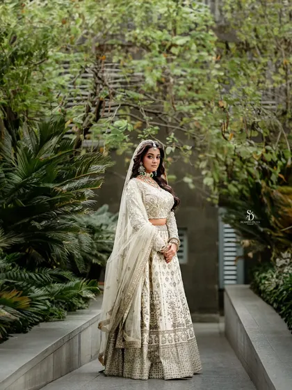 A full-length shot of a model in a magnificent white and gold lehenga. The outdoor garden path provides a beautiful, natural runway for this grand bridal outfit.