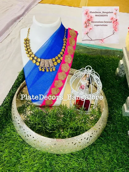 I also create displays for non-food gifts. Here, a beautiful blue and pink saree and a traditional necklace are elegantly presented on a mannequin, set within a decorative silver tray for a wedding ceremony.