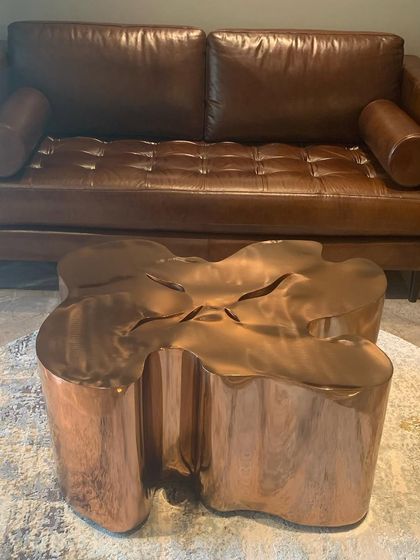 A rich, tan leather sofa paired with a sculptural copper coffee table, a classic combination of warm and cool materials.