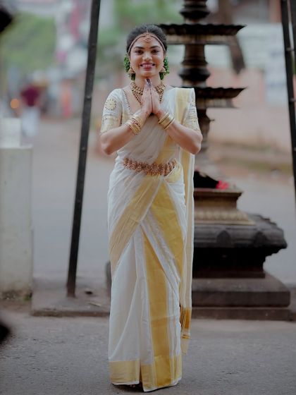 A portrait of the bride in a classic Kerala kasavu saree, her hands joined in a respectful 'namaste' at the temple entrance.