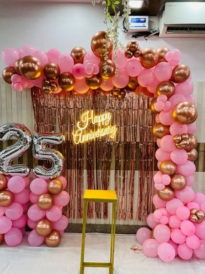 A beautiful 25th anniversary setup featuring a rose gold fringe curtain and a pink and metallic balloon arch. The large silver foil "25" balloons clearly mark the milestone, making it perfect for photos.