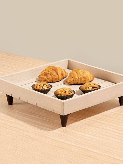 A square wooden serving tray with croissants and tarts, shot in a clean, minimalist style.