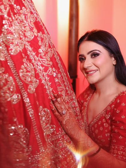 A close up of the bride, touching her lehenga. The red lighting adds to the dramatic and romantic feel.
