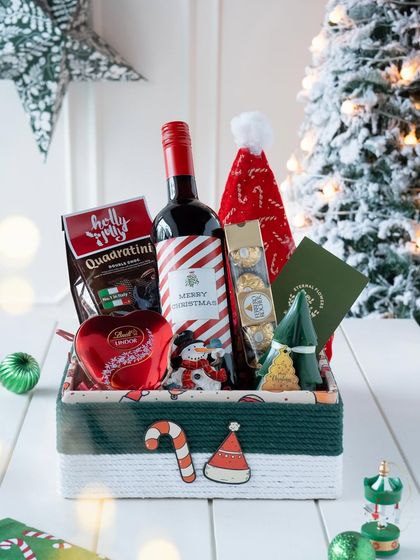 My 'Jolly Feast' Christmas hamper, featuring a custom-labeled wine bottle, chocolates, and festive ornaments in a green and white themed box.
