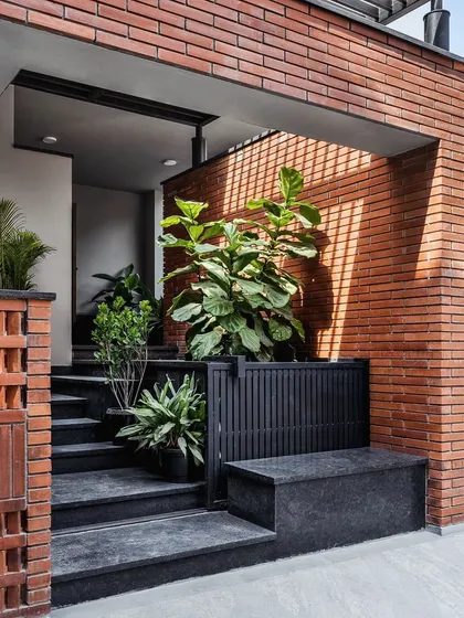 The entrance to this home features a crisp combination of exposed brick and lush greenery. A large Fiddle-Leaf Fig in a built-in planter creates a welcoming and natural first impression.