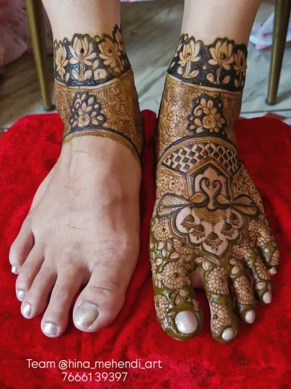 This image shows the process of creating a symmetrical bridal foot design. You can see the finished art on one foot and the other in progress, highlighting the bold lines and lotus borders that frame the design.