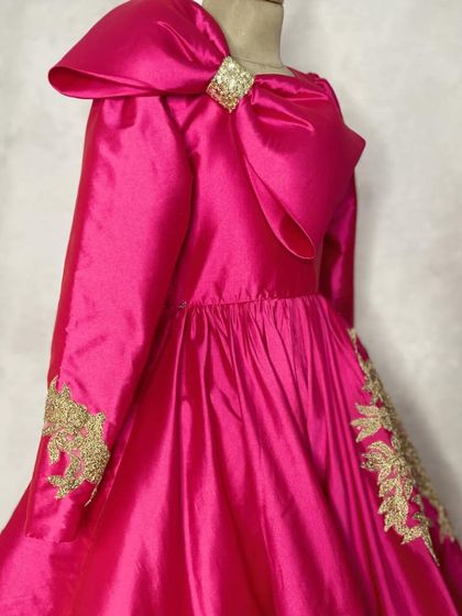 This stunning magenta gown is designed for the perfect twirl at any wedding reception. It features dramatic sleeves, a large shoulder bow, and delicate gold embroidery on the cuffs and skirt.