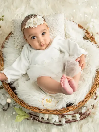 A sweet baby girl in a white lace outfit, showing off her cute little feet while sitting in a basket.