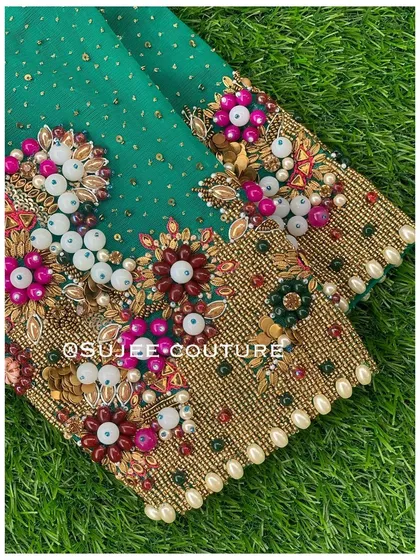 A detailed shot of a heavily embellished sleeve cuff. This design features a dense pattern of 3D floral motifs created with beads, sequins, and zardozi on a rich green fabric.