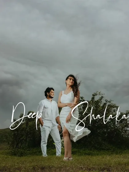 A stylish pre-wedding portrait of a couple standing in a green field, with a dramatic, overcast sky adding to the mood.