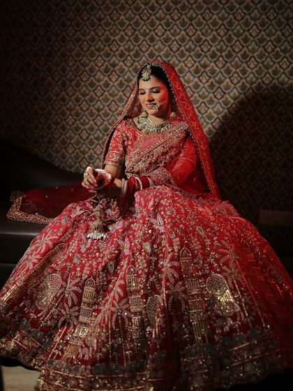 A full-length shot showing the complete bridal look. The makeup perfectly complements her magnificent red lehenga.