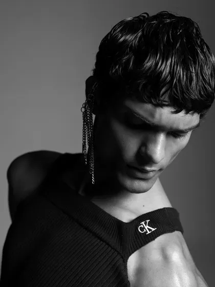 A detailed shot focusing on an unconventional way of styling a Calvin Klein top. The addition of a chain earring adds an edgy, editorial element to the overall look.