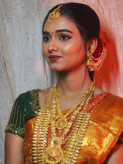 A side profile of Soundariya's look, showing the elegant hair bun adorned with red flowers, perfectly complementing her green blouse and gold jewelry.