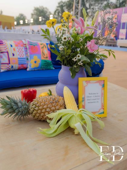 A creative centerpiece featuring a whole pineapple, corn on the cob, and bell peppers alongside a floral arrangement. This highlights the use of edible, zero-waste decor.
