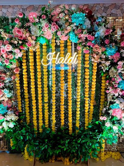 A closer look at the details of the multi-colored Haldi backdrop. The mix of flowers and the bright neon sign creates a lively and photogenic setting.