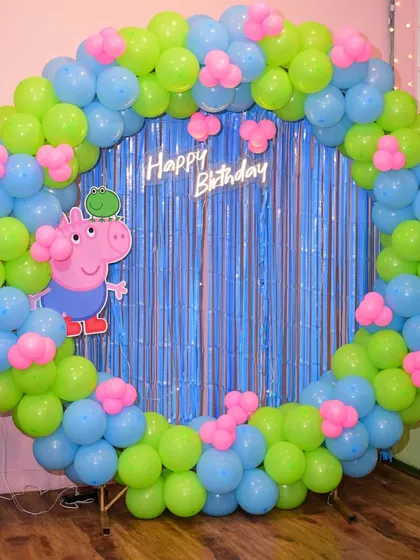 George Pig makes an appearance in this fun Peppa Pig party setup, complete with a blue, green, and pink balloon arch.