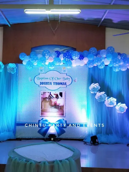 A blue-themed baptism stage decoration. The setup uses blue drapes and lighting, with a balloon arch and paper flowers creating a serene ambiance.