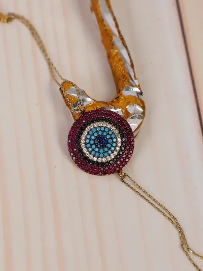 A close-up of a detailed evil eye bracelet, styled on a piece of driftwood. This rustic, natural setting makes the jewelry's colors and crystals pop.