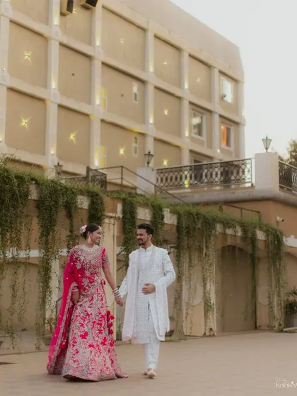 A classic walking portrait of the couple in front of a beautiful building, showcasing their stunning wedding outfits.