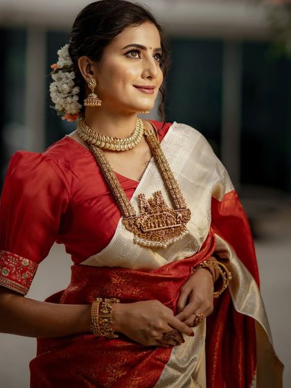 This is a look of pure bridal grace. Our model is adorned in a classic off-white and red Kancheevaram silk saree, complete with traditional temple jewelry and fragrant jasmine in her hair.