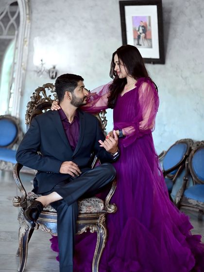 A regal and intimate pre-wedding portrait. The deep purple gown with sheer sleeves looks luxurious and romantic in this elegant indoor setting.