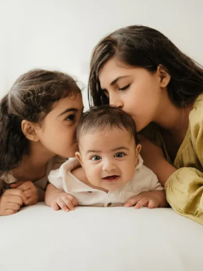 Two sisters kiss their baby brother's cheeks. This is a heartwarming portrait that perfectly captures sibling affection.
