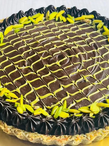 A close-up of the Dubai Chocolate Cheesecake Tart, highlighting the intricate chocolate work and the sprinkle of bright green pistachios.