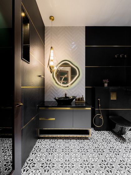 A bold and dramatic bathroom featuring black and gold accents, patterned floor tiles, and a unique illuminated mirror. This design proves that bathrooms can be showstoppers.