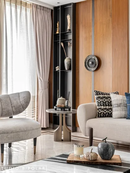 A detail shot of the living room corner, where a sculptural side table sits next to a comfortable armchair. The wood-paneled wall and tall display niche add verticality and texture.