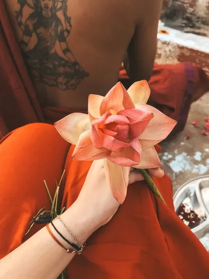 A student holds a lotus flower during a ceremony, seated next to another with a beautiful back tattoo of a deity. This image shows the blend of personal expression and shared tradition at our ashram.