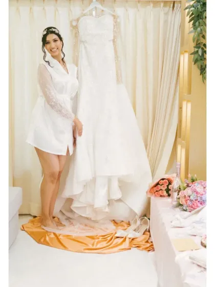 The bride in her robe, standing proudly next to her beautiful wedding gown. This is a classic and elegant getting-ready shot.